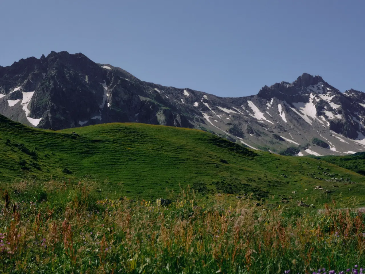 Green alpine slope beneath a rugged mountain ridge and blue sky