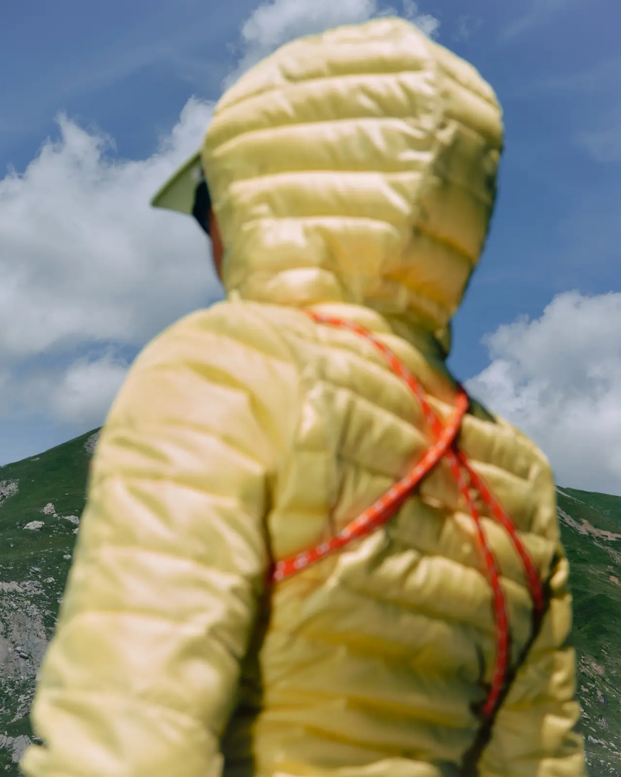 Rear view of a hiker in a pale yellow jacket with an orange cord across the back