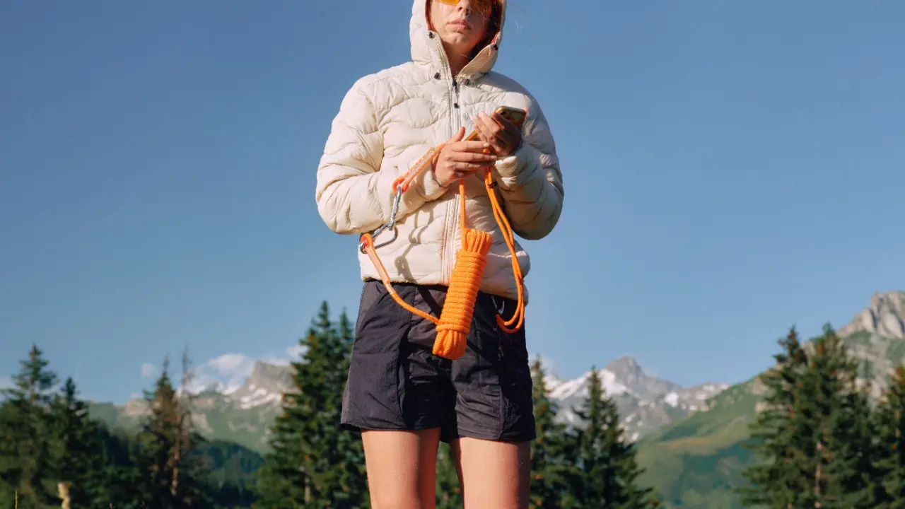 Hiker holding a phone and a coil of orange cord in front of mountain scenery